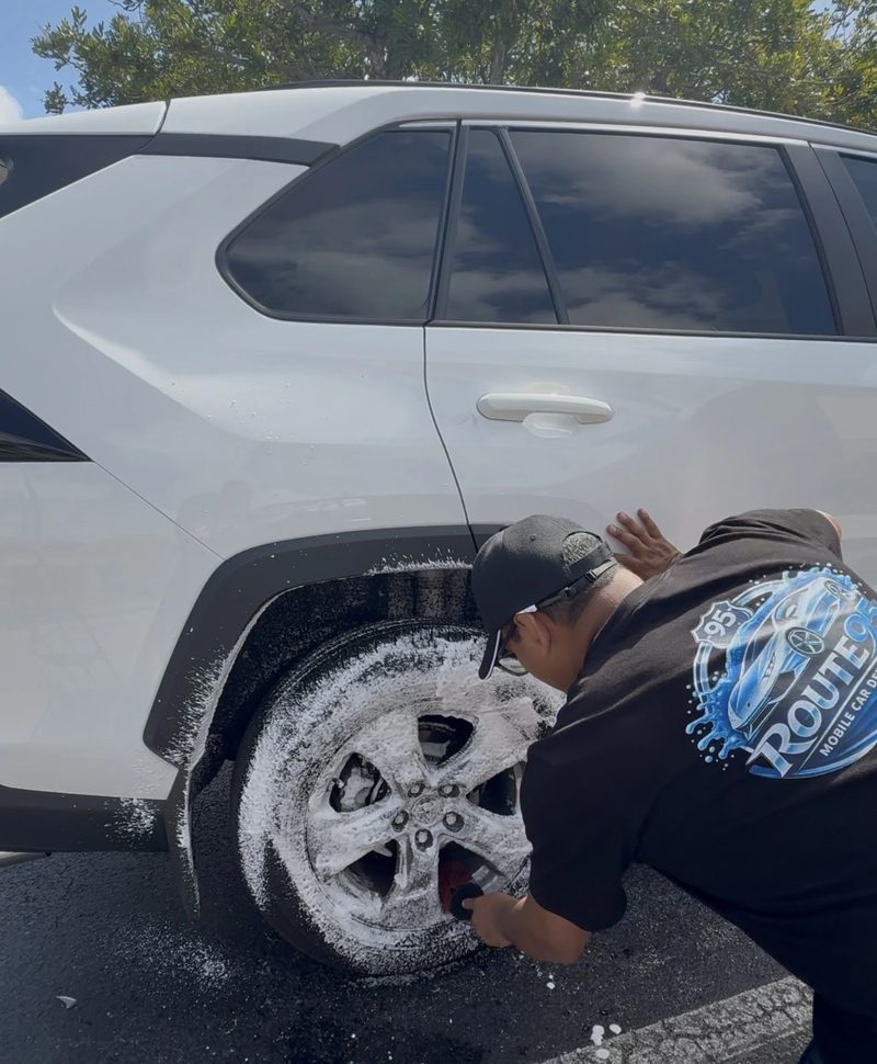 Route95 technician hand-scrubbing brake dust off an alloy rim with foaming wheel cleaner during a mobile wheel cleaning service in Fort Lauderdale